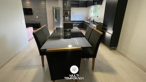 A modern kitchen with a central island, black cabinetry, and a dining area with a large table and chairs. - Refúgio Menegaz - Governador Celso Ramos - SC (Governador Celso Ramos)