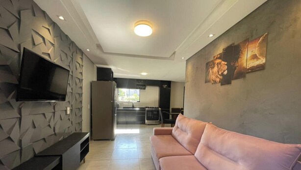 A modern living room with a flat-screen TV, a pink sofa, and a kitchen in the background. - Refúgio Menegaz - Governador Celso Ramos - SC (Governador Celso Ramos)