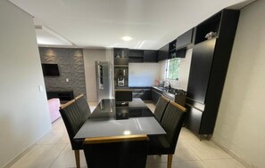A modern kitchen with a central island, black cabinetry, and a dining area with a large table and chairs. - Refúgio Menegaz - Governador Celso Ramos - SC (Governador Celso Ramos)