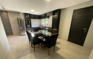 A modern kitchen with a dining area, featuring a black and white color scheme, a refrigerator, oven, and a black door. - Refúgio Menegaz - Governador Celso Ramos - SC (Governador Celso Ramos)