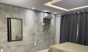 A modern bedroom with a large bed, a wall-mounted air conditioning unit, a mirror, and a curtain. - Refúgio Menegaz - Governador Celso Ramos - SC (Governador Celso Ramos)