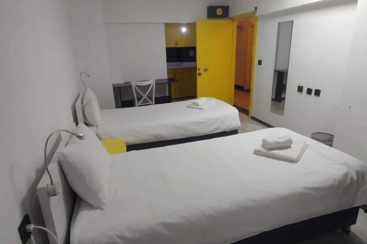 A hotel room with two beds, a desk, a chair, and a small kitchenette.