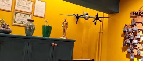 A room with a yellow wall, two clocks, a small airplane model, and a sign reading "rota gezgin".