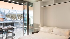 Moderni hotellihuone, jossa on suuri sänky, lasiseinä ja näkymä ulkoilma-ateriointialueelle.