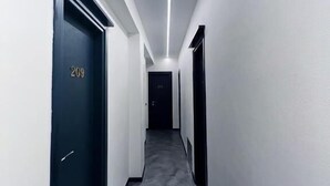 Un pasillo estrecho, bien iluminado, con piso oscuro y paredes blancas.