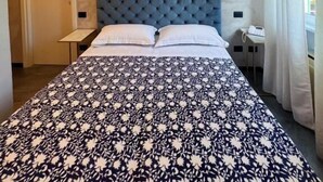 Una habitación de hotel con una cama grande, cabecera capitonada, mesita de noche y una ventana con cortinas.