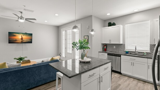 A modern kitchen with white cabinets, a granite countertop, and a built-in dishwasher. - Canopy Couplet | 2 Upscale Apts In Prime Location (Safety Harbor)