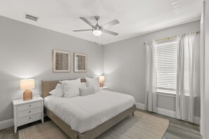 Un dormitorio con una cama, mesitas de noche, un ventilador de techo y una ventana con cortinas.
