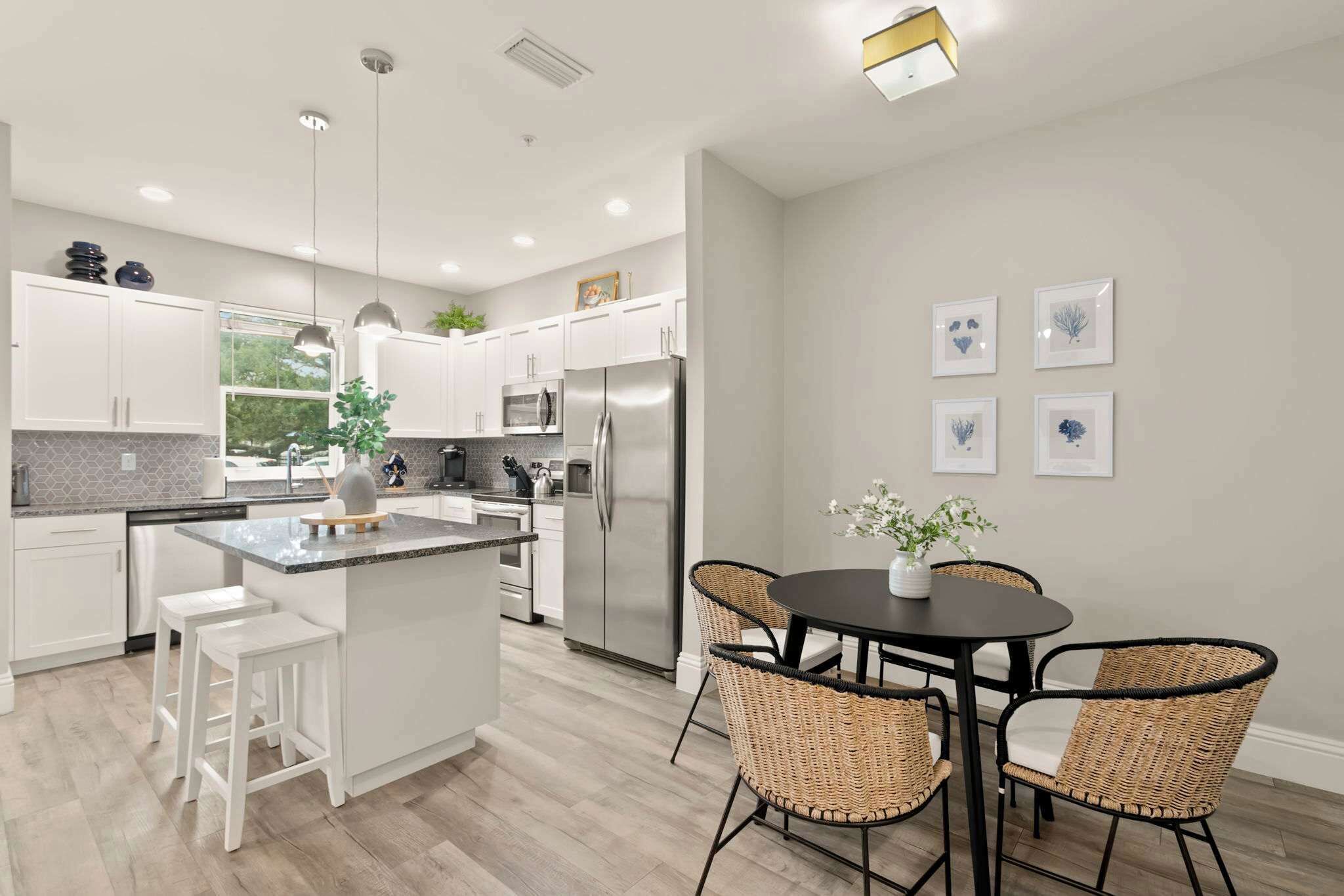 A modern kitchen with white cabinets, stainless steel appliances, a central island, and a dining area with wicker chairs.