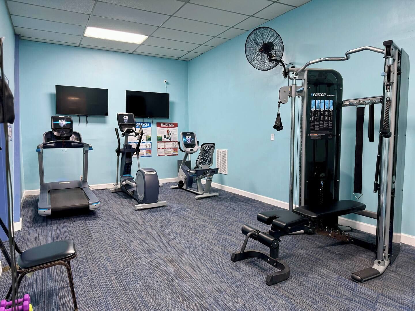 Un gimnasio con cintas de correr, elípticas, una banca y una estructura para sentadillas.