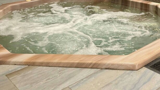 A hot tub with a stone wall and wooden door in the background. - 2120  Hot tub, sauna & more resort amenities Beautifully remodeled, 1st-floor (Beech Mountain)
