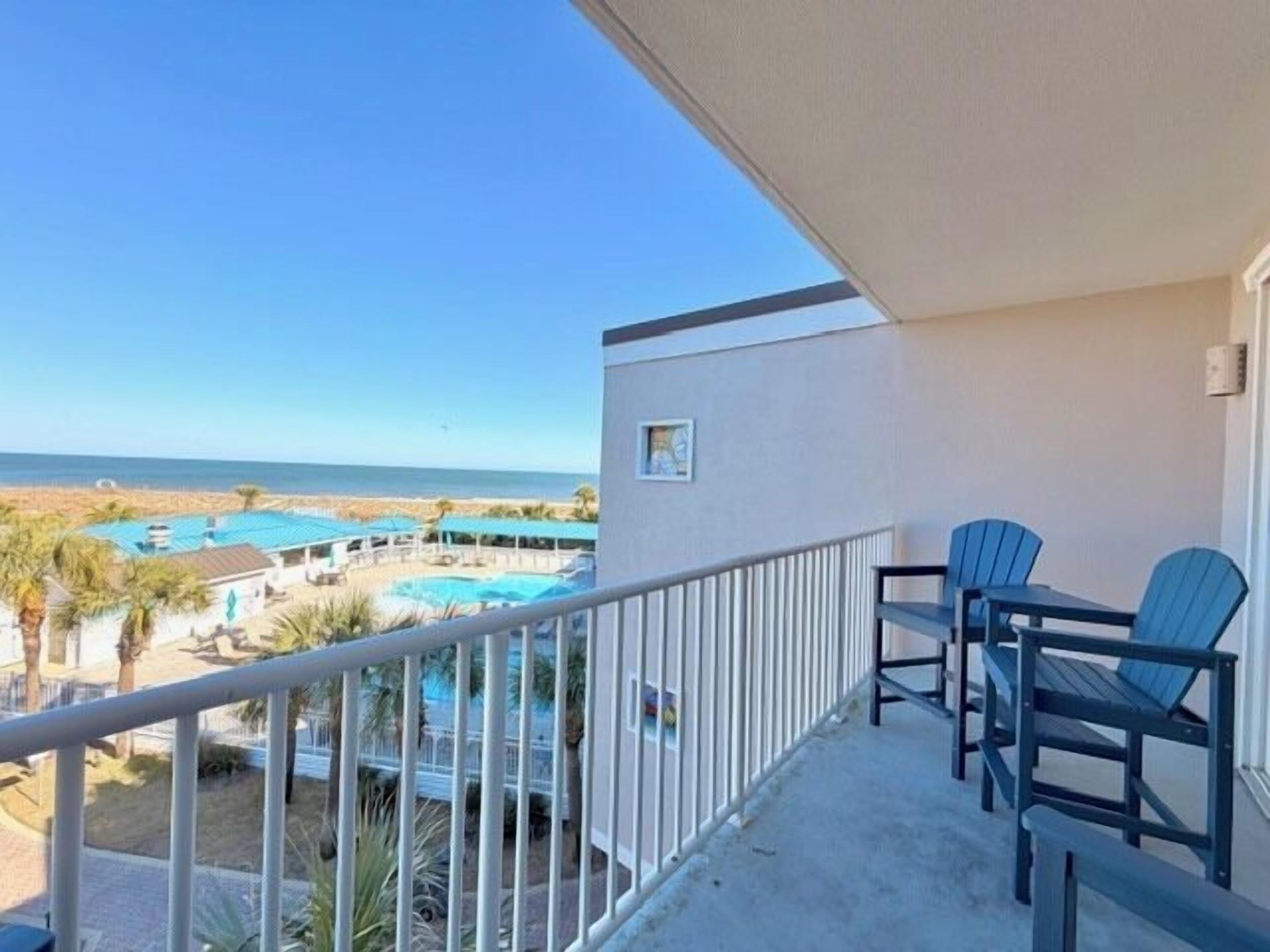A balcony with a view of a beach and a pool area.