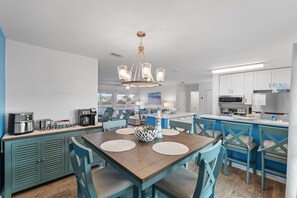 A modern kitchen with white cabinets, a central island, and a dining area with blue chairs and a wooden table. - Coastal 3BR Retreat at Sandpiper Cove | Sleeps 10 (destin)