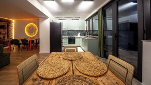 Una cocina moderna con comedor, que presenta una mesa de madera con individuales tejidos, una pared de ladrillo decorativa y vistas a través de un ventanal.
