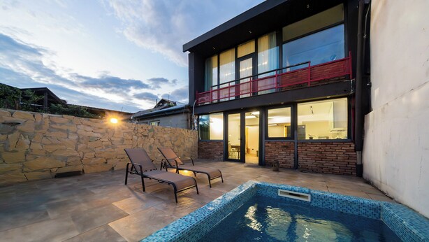 Una casa moderna con piscina, muro de piedra y dos sillones de descanso.