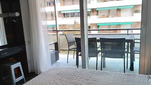 A room with a bed, a small stool, a table with chairs, and a view of a balcony with a table and chairs. - KATALIN (Lloret de Mar)