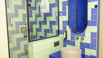 Une salle de bain avec un mur recouvert de carreaux bleus et verts, un miroir rond et un lavabo doté d’un plan de travail bleu.