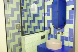 A bathroom with a blue and green tiled wall, a round mirror, and a sink with a blue countertop.