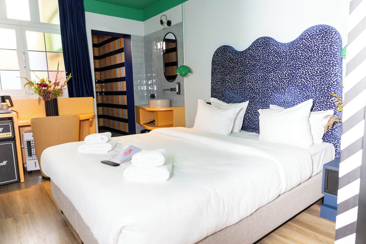 A hotel room with a large bed, a desk with a computer, a bathroom with a sink and mirror, and a view of the outside.