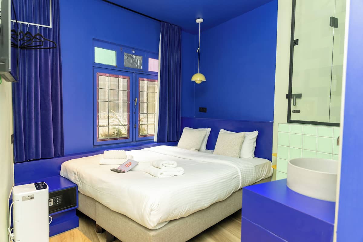 A hotel room with a large bed, a bedside table, a window with curtains, and a bathroom with a sink and mirror.