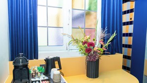 A hotel room with a window, a coffee maker, a tray with coffee cups, a vase with flowers, and a blue curtain. - P6 Antwerp (Antwerp)