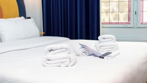 A neatly made bed with white linens, a remote control, and rolled towels on a hotel room. - P6 Antwerp (Antwerp)
