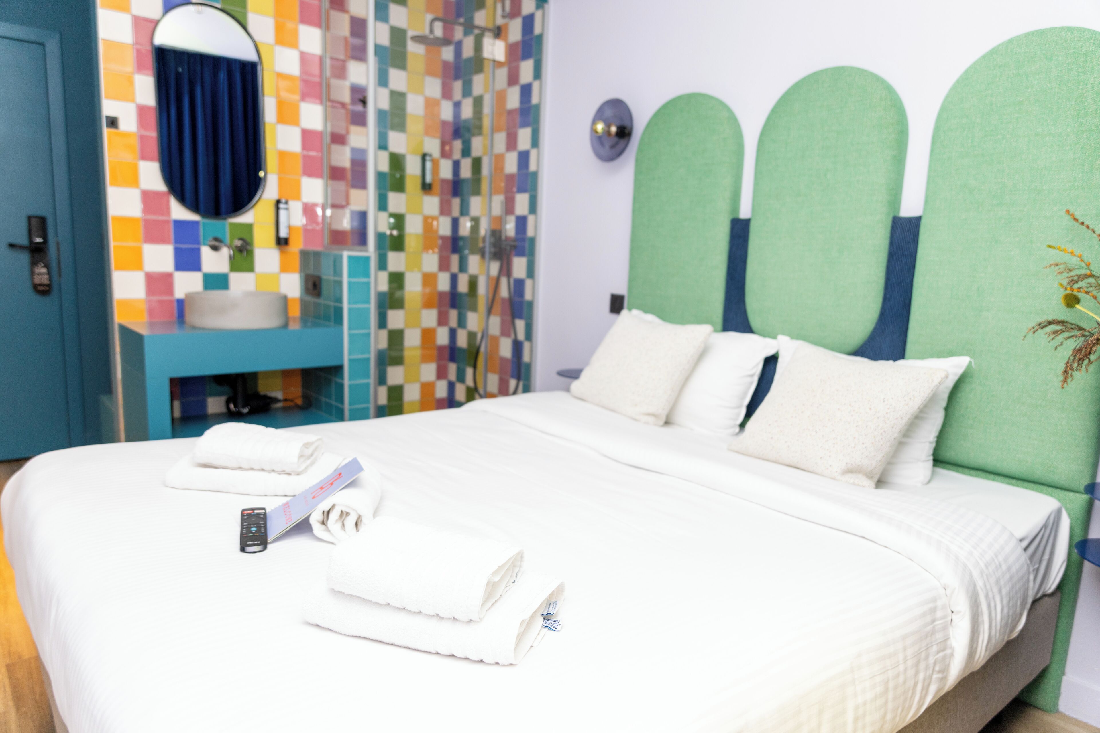 A hotel room with a bed, a bathroom with a colorful tile wall, and a green headboard.