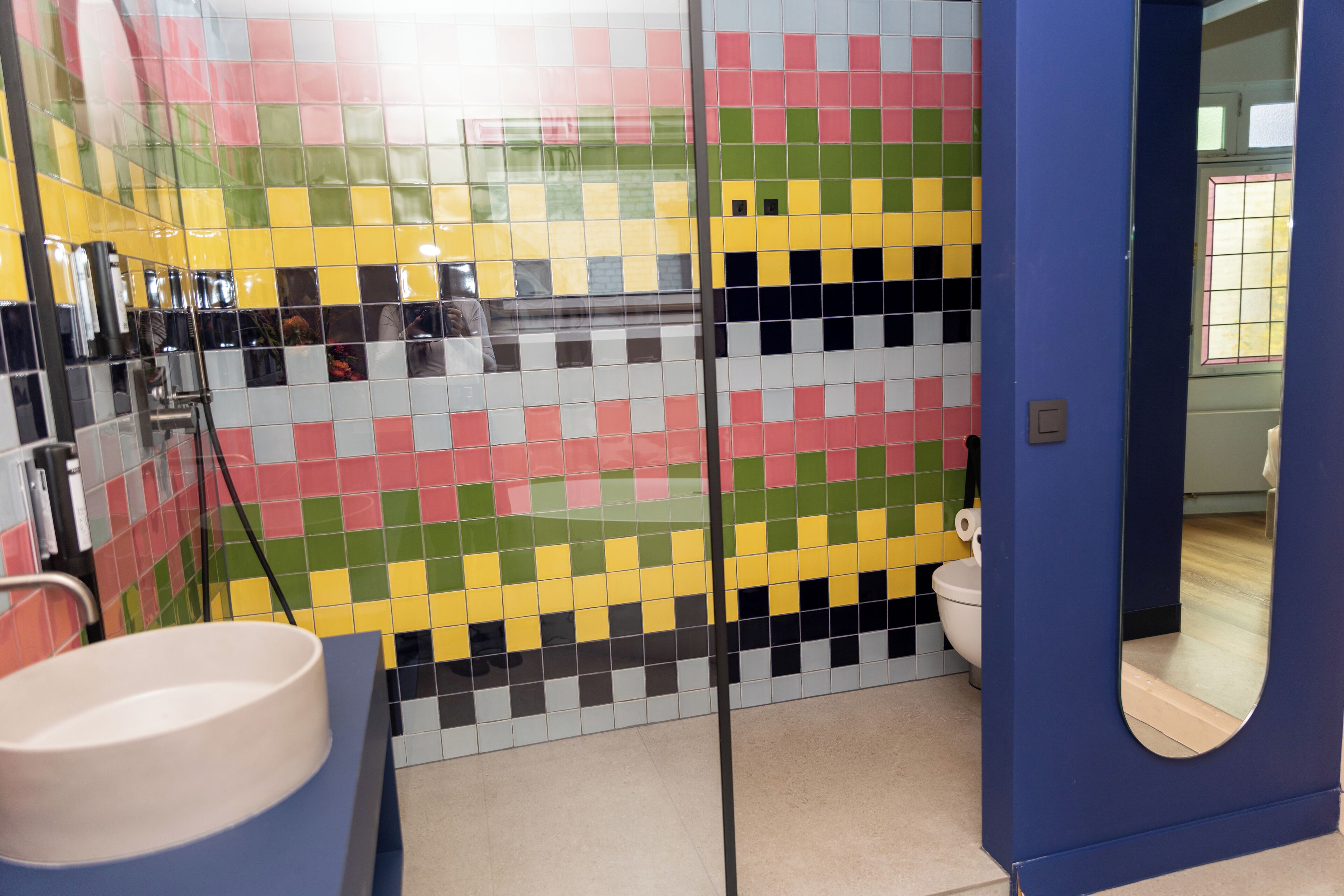 Un baño con pared de mosaicos de colores, un lavamanos blanco y una puerta azul.