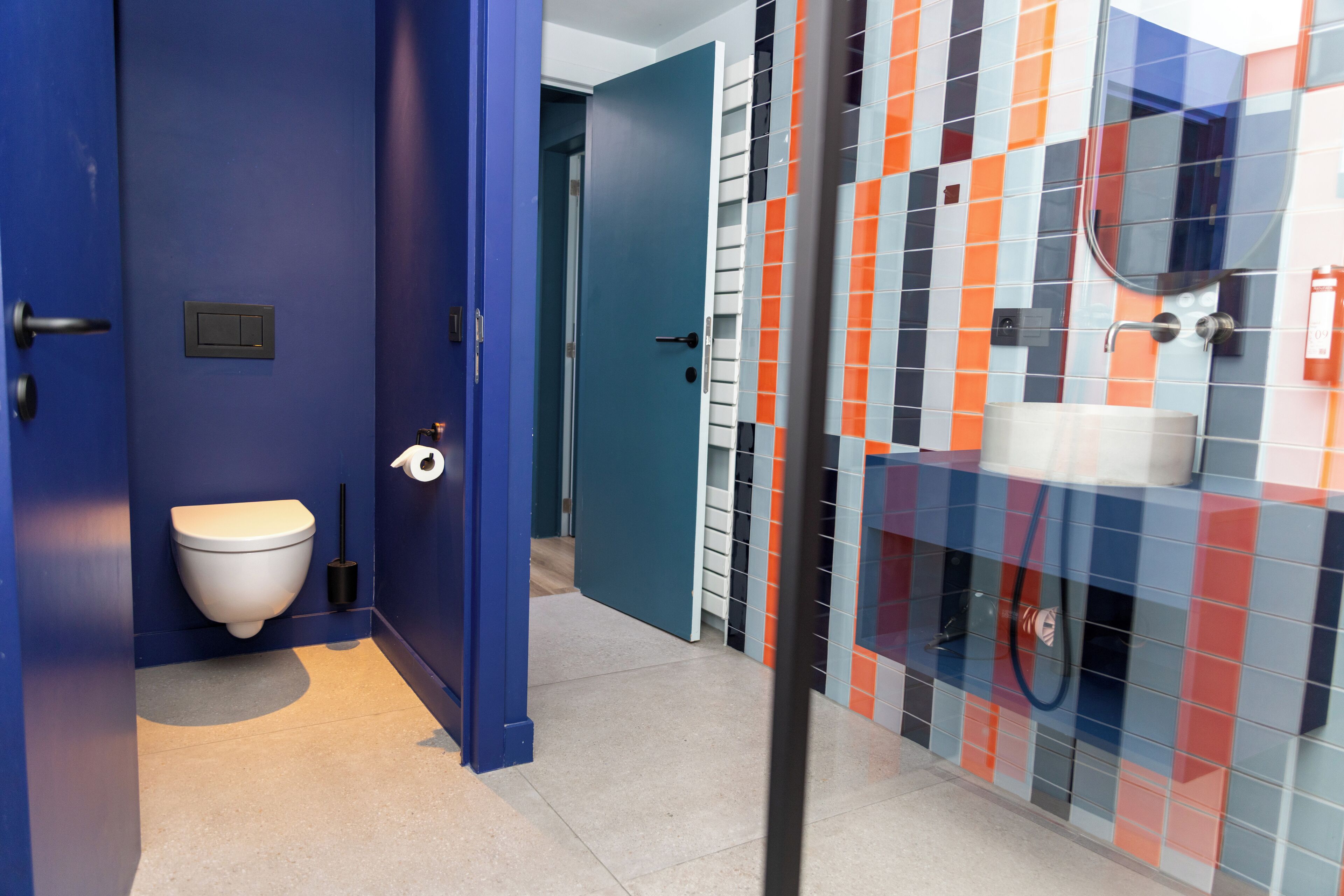 Ein Badezimmer mit blauer Tür, Toilette in Weiß und einer gefliesten Duschkabine.