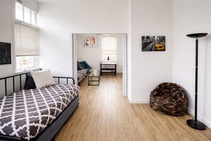 A bedroom with a bed, a chair, a small table, and a floor lamp. - Short & Long-Term Rentals | Monthly Discount (Cheltenham Township)