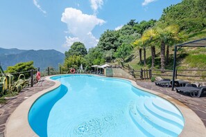 A swimming pool with a curved edge, surrounded by a stone deck and a wooden fence. - Room 'Stanza 2' with Lake View, Wi-Fi and Air Conditioning (Marone)