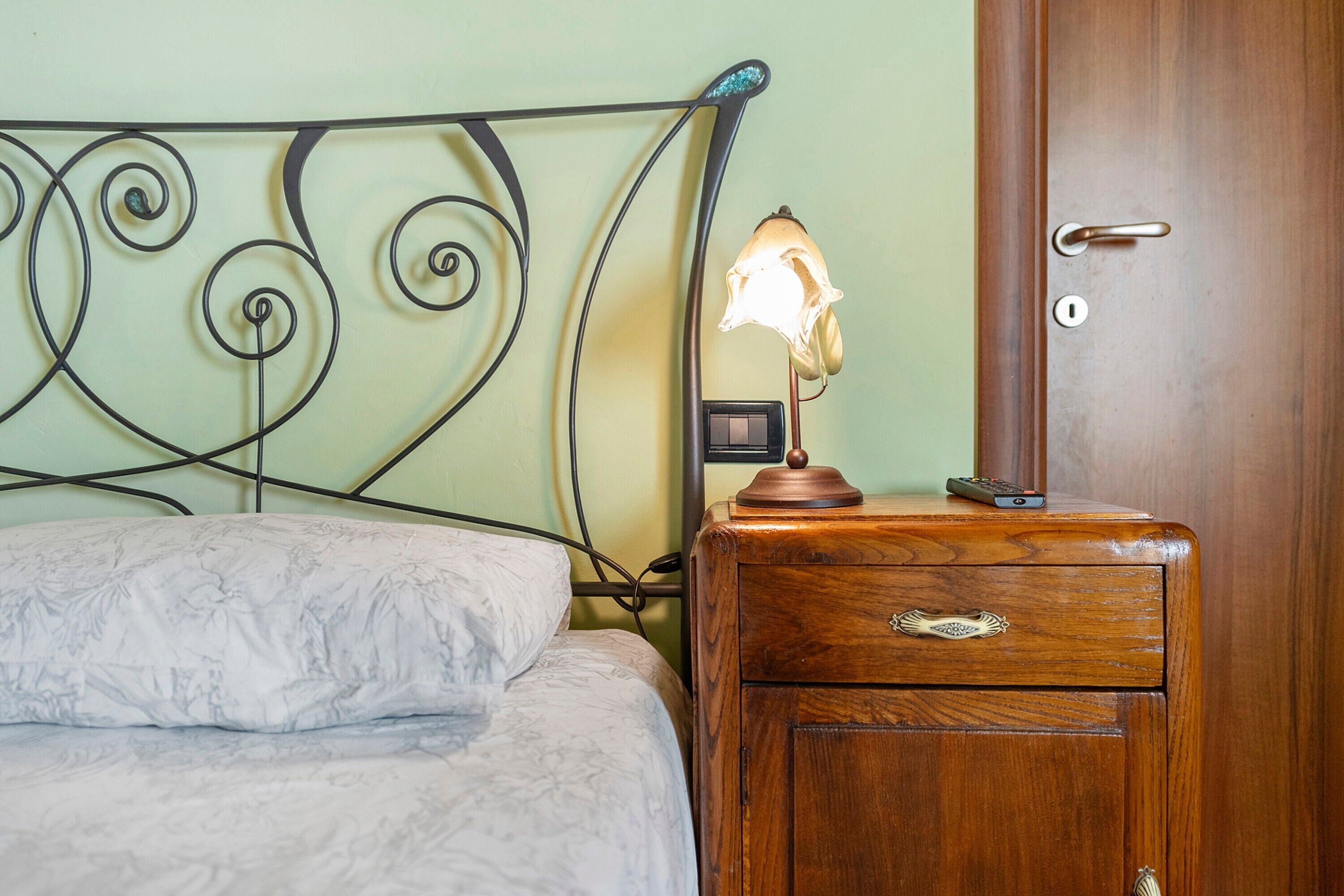 Uma cama com cabeceira, uma mesa de cabeceira com abajur e uma porta de madeira.