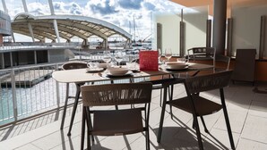 A dining area with a view of a marina, featuring a table set with plates, glasses, and a red menu stand. - Waterfront Suite by Wonderful Italy (Genoa)
