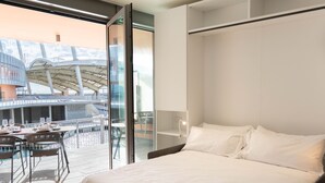 A modern hotel room with a large bed, a glass wall, and a view of an outdoor dining area. - Waterfront Suite by Wonderful Italy (Genoa)