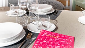 A neatly set dining table with plates, glasses, and cutlery, a red menu, and a modern kitchen in the background. - Waterfront Suite by Wonderful Italy (Genoa)