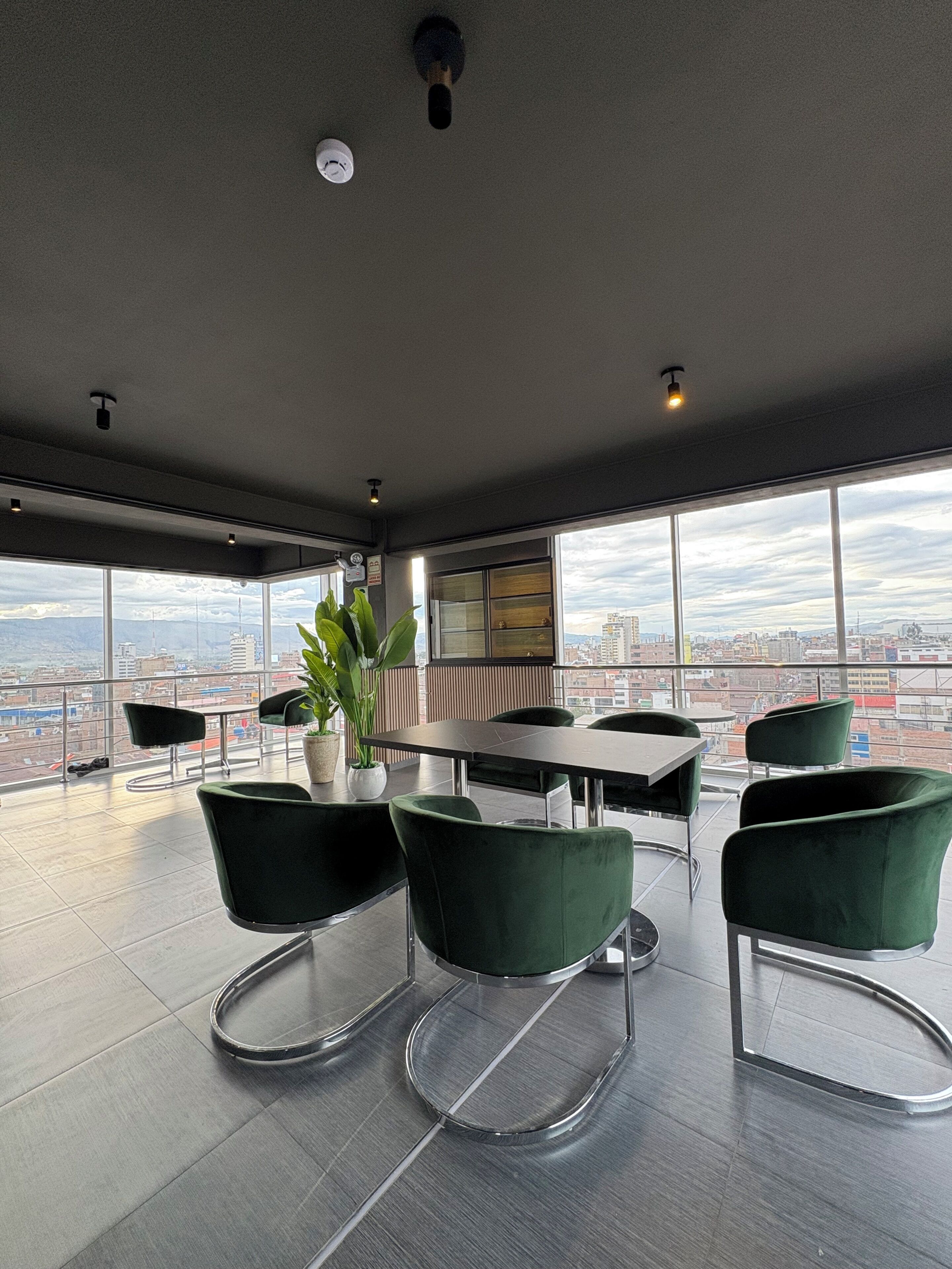 A modern conference room with a panoramic city view, a round table, and green upholstered chairs.