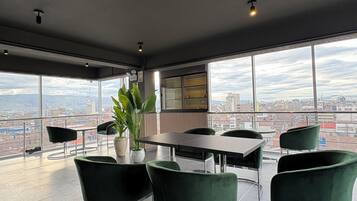 A modern conference room with a panoramic city view, a round table, and green upholstered chairs.