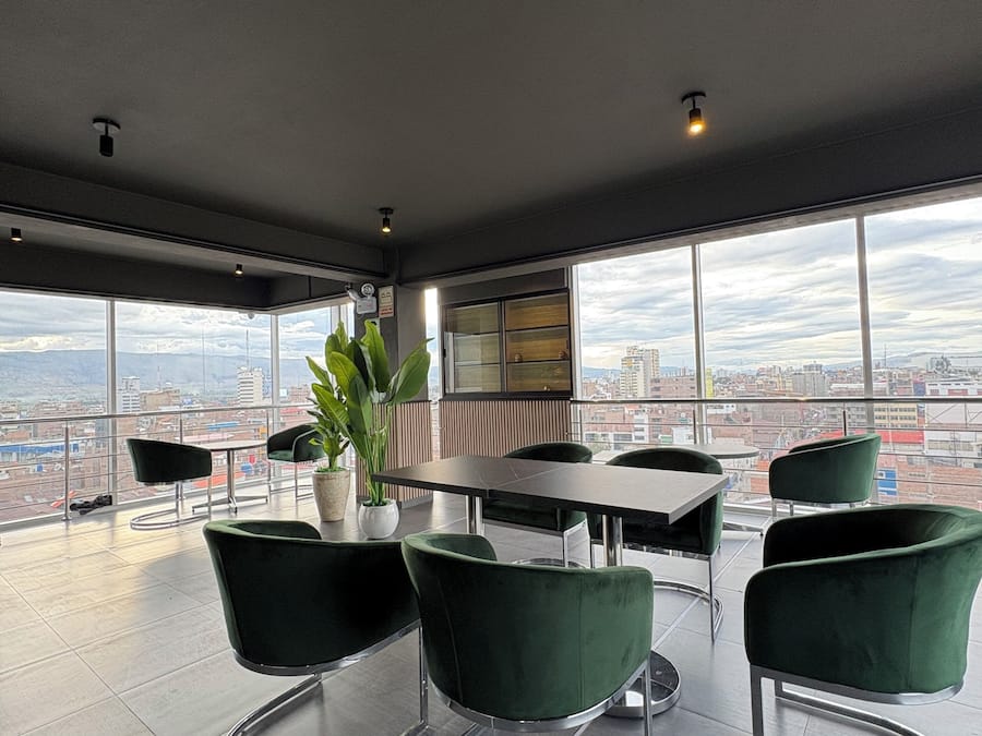 A modern conference room with a panoramic city view, a round table, and green upholstered chairs.