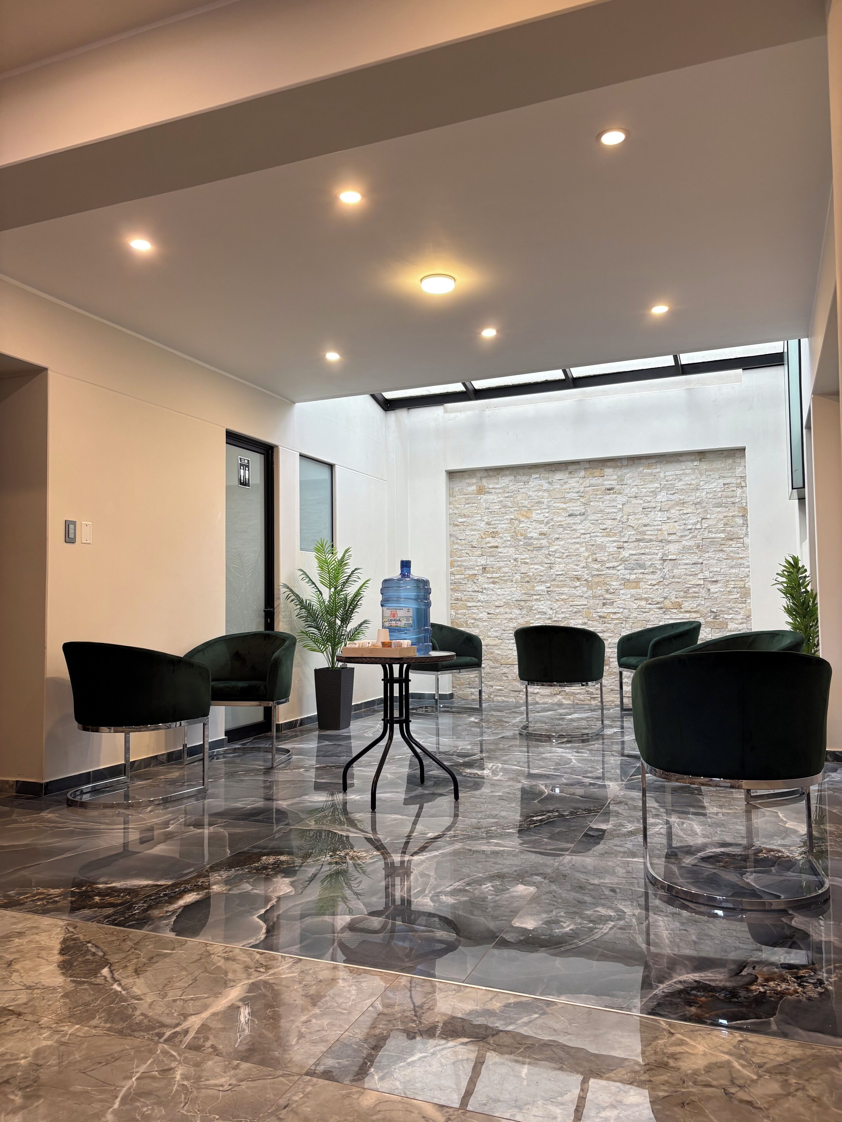A modern interior with a stone wall, a water dispenser, and four dark chairs around a small table.