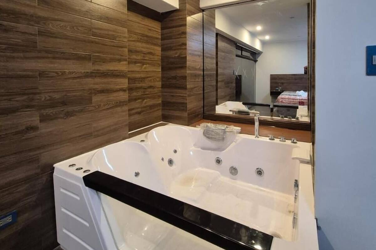 A modern bathroom with a large white bathtub, wooden wall paneling, and a mirror reflecting the room.