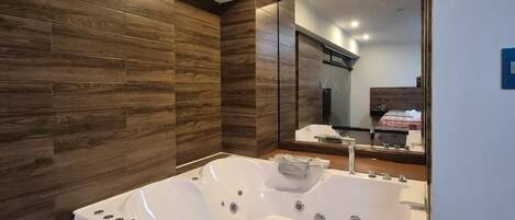 A modern bathroom with a large white bathtub, wooden wall paneling, and a mirror reflecting the room.