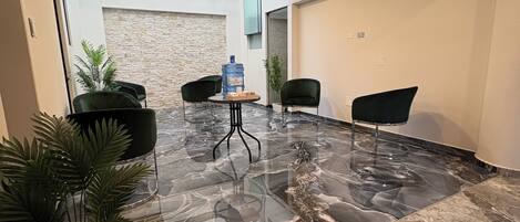 A modern lobby with marble flooring, a large water dispenser, and several black chairs.