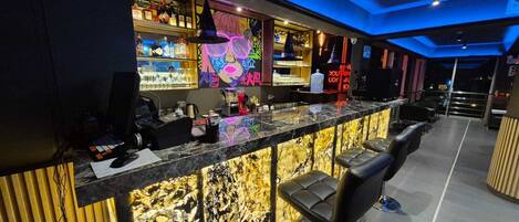 A bar area with a marble countertop, bar stools, and shelves stocked with bottles.