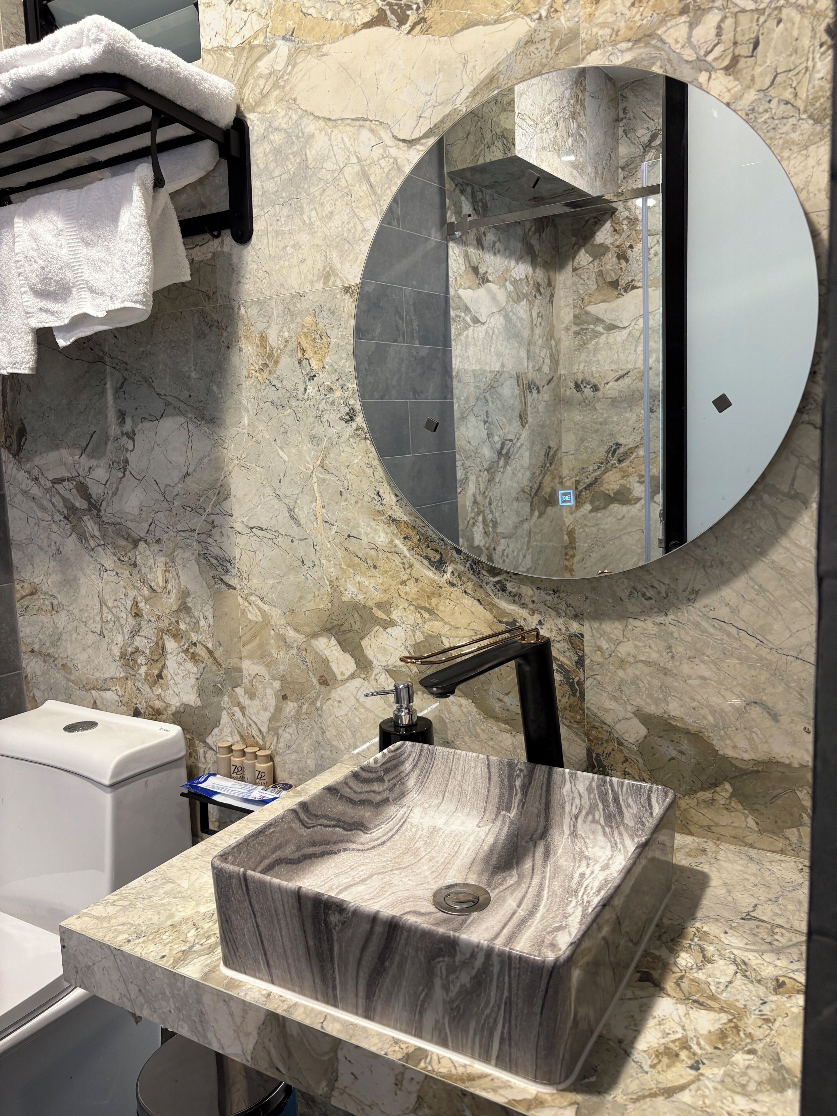 Un baño con encimera de mármol, lavamanos de pedestal, espejo redondo y toallero.