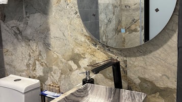 Un baño con encimera de mármol, lavamanos de pedestal, espejo redondo y toallero.
