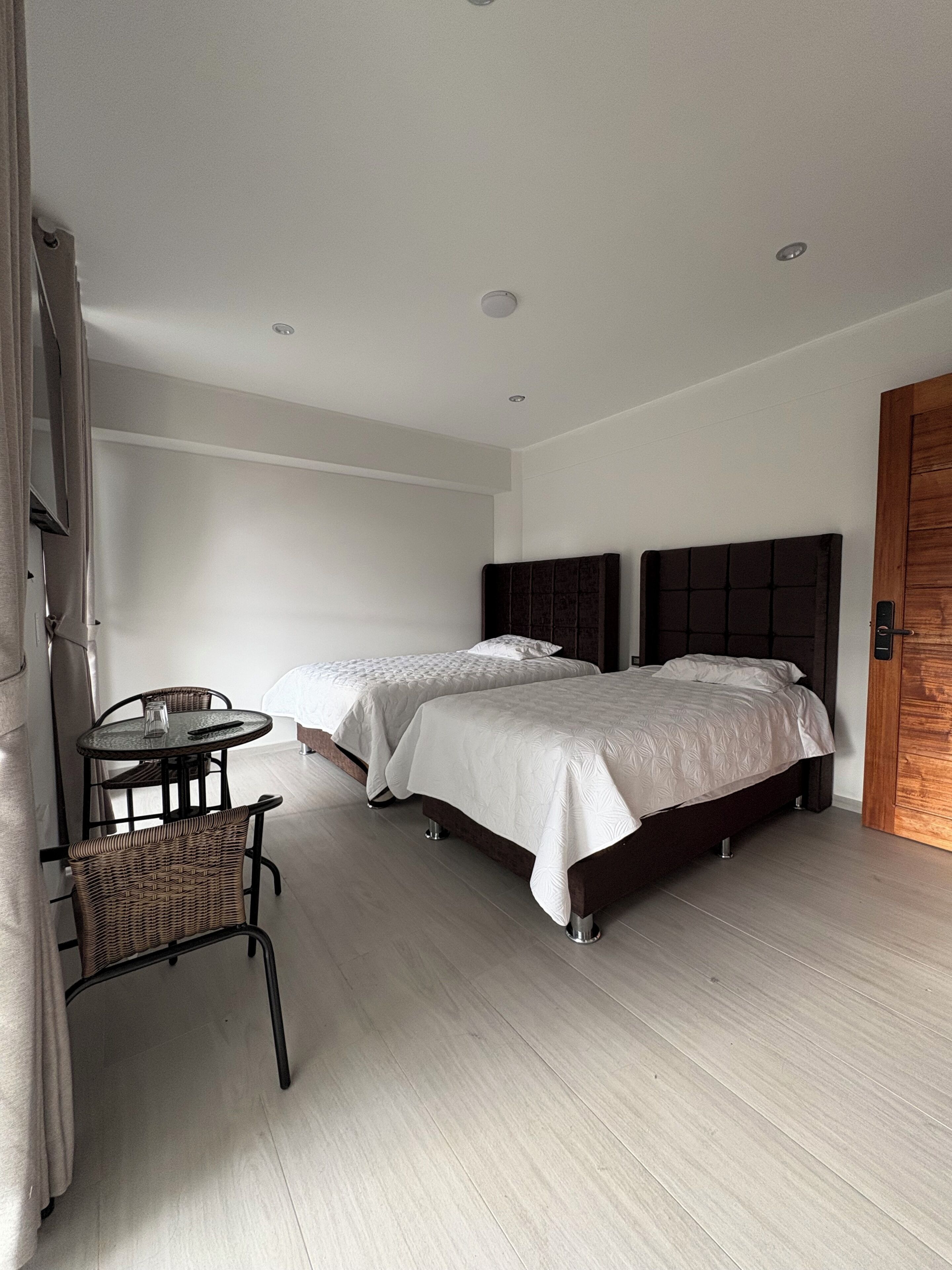 Ein Hotelzimmer mit zwei Betten, einem kleinen Tisch, einem Stuhl und einer Holztür.