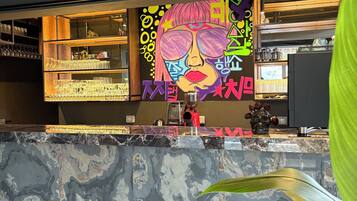 Una zona de bar con encimera de mármol, estanterías con copas y un mural colorido.