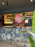 Una zona de bar con encimera de mármol, estanterías con copas y un mural colorido.