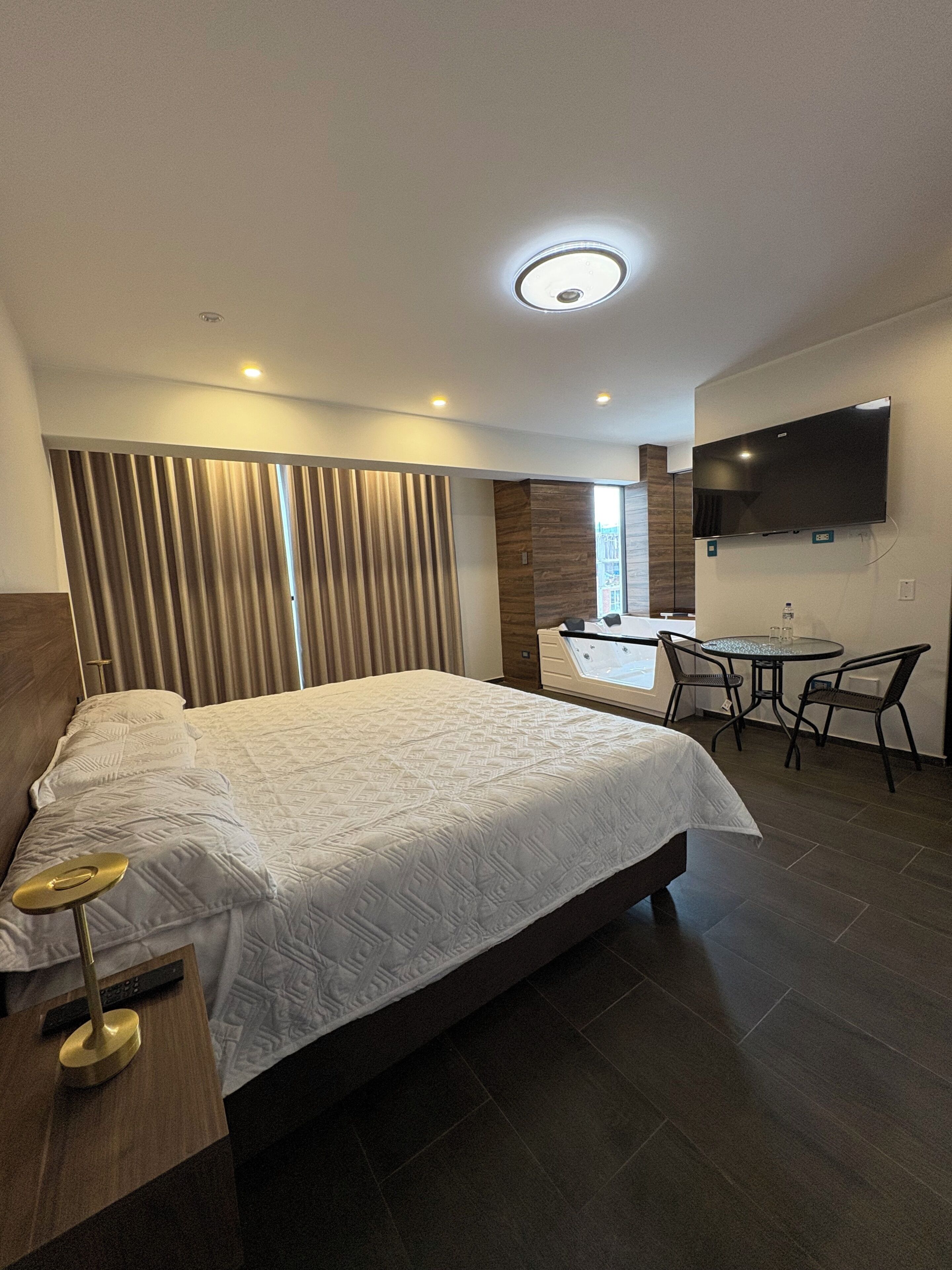 A modern hotel room with a large bed, a desk, a chair, a TV, and a bathroom with a bathtub.