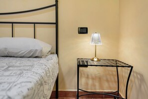 A single bed with a patterned bedspread, a bedside table with a lamp, and a wall-mounted switch. - Room 'Stanza 4' with Mountain View, Wi-Fi and Air Conditioning (Marone)